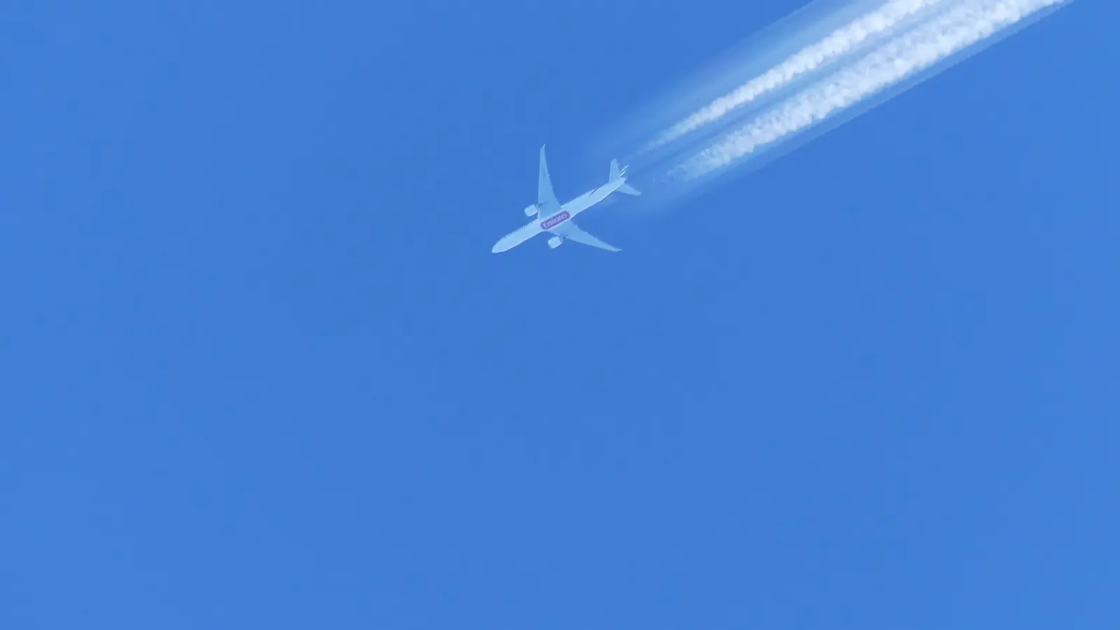 Commercial aircraft crosses a blue sky while leaving two white condensation trails.